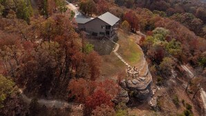 A large house surrounded by autumn foliage, with a dirt path leading to a circular stone seating area. - Sycamore Ranch - Private MTB Trails - Hot tub! (Eureka Springs)