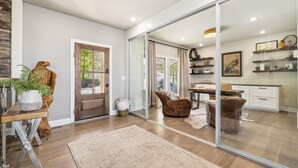 A modern interior with a wooden floor, a large mirror reflecting a kitchen area, a wooden statue, and a potted plant. - Sycamore Ranch - Private MTB Trails - Hot tub! (Eureka Springs)