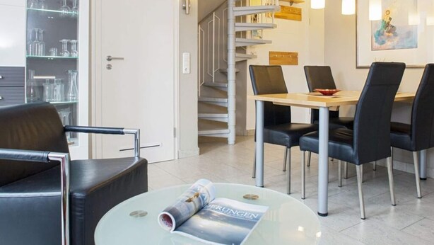 A modern interior with a dining area, a spiral staircase, and a glass table with a magazine. - Vakantieappartement "ambiente" (Sylt)