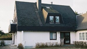 A two-story house with a sloped roof, a visible chimney, and a small window. - Vakantieappartement "ambiente" (Sylt)