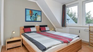 A bedroom with a sloped ceiling, a bed with a striped bedspread, a nightstand with a lamp, and a window with curtains. - Vakantieappartement "ambiente" (Sylt)