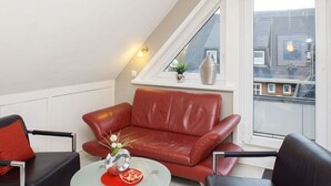 A modern living room with a red leather sofa, a glass coffee table, and two black armchairs. A small plant and a vase are on the windowsill. - Vakantieappartement "ambiente" (Sylt)