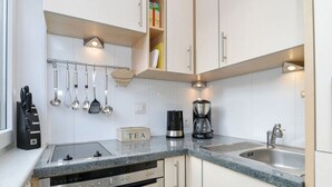 A modern kitchen with white cabinets, a granite countertop, a coffee maker, a kettle, and a tea box. - Vakantieappartement "ambiente" (Sylt)