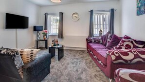 A living room with a sofa, a television, a clock, and a window with curtains. - Bridge House in Skinningrove (Saltburn-by-the-Sea)