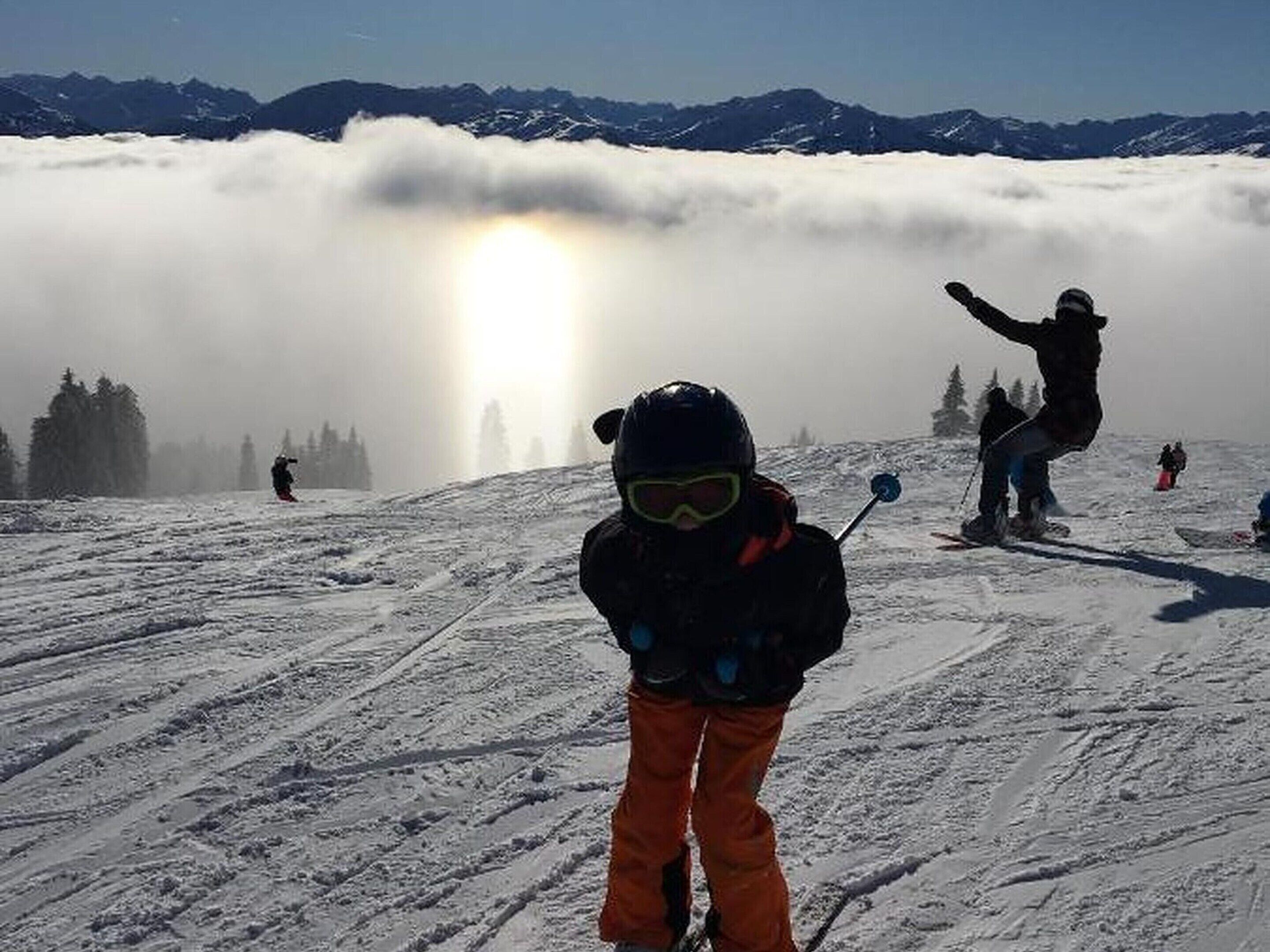 A snowy ski slope with skiers and a child in the foreground.
