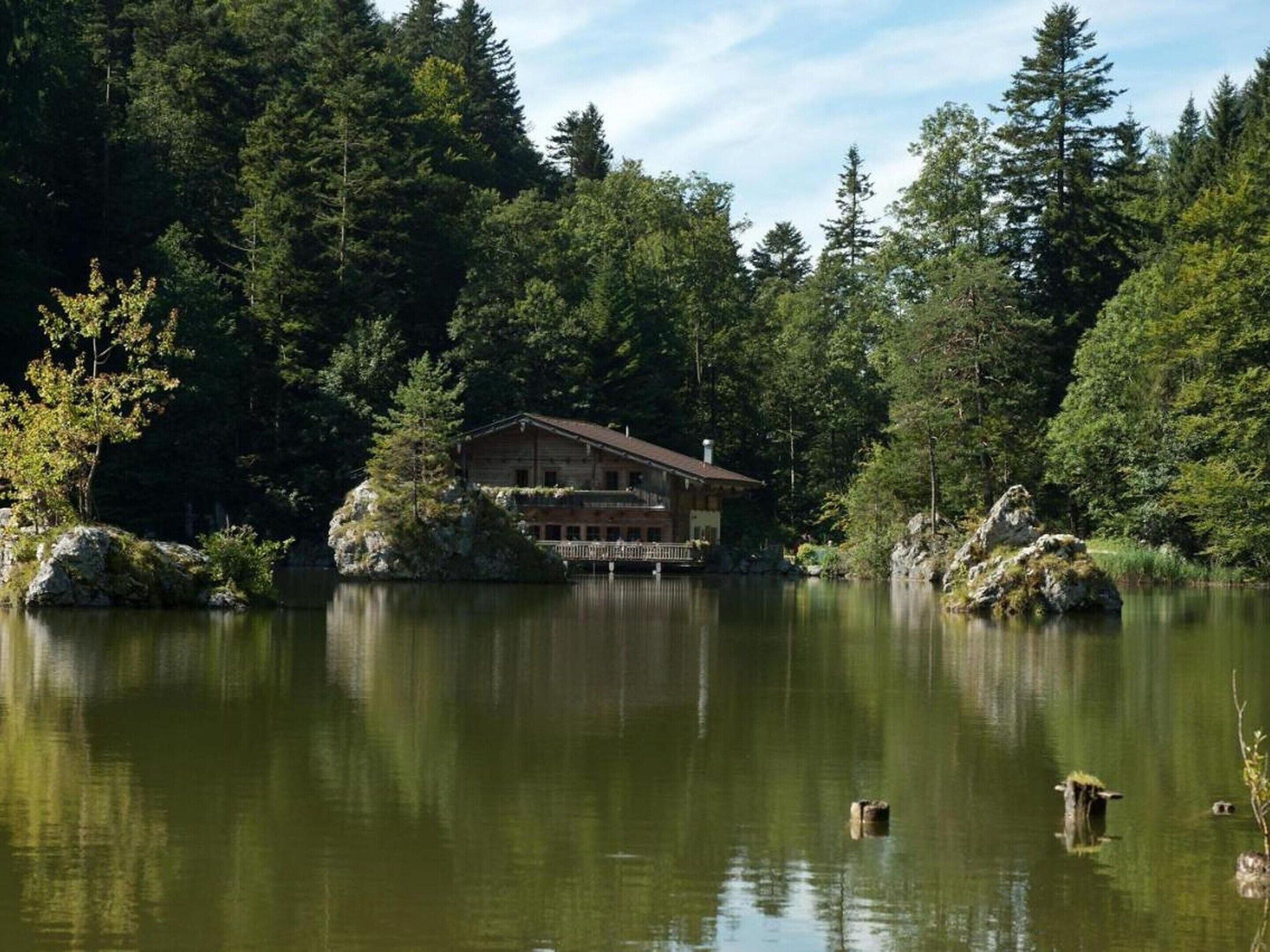 A lodge with a large deck overlooking a lake, surrounded by dense forest.
