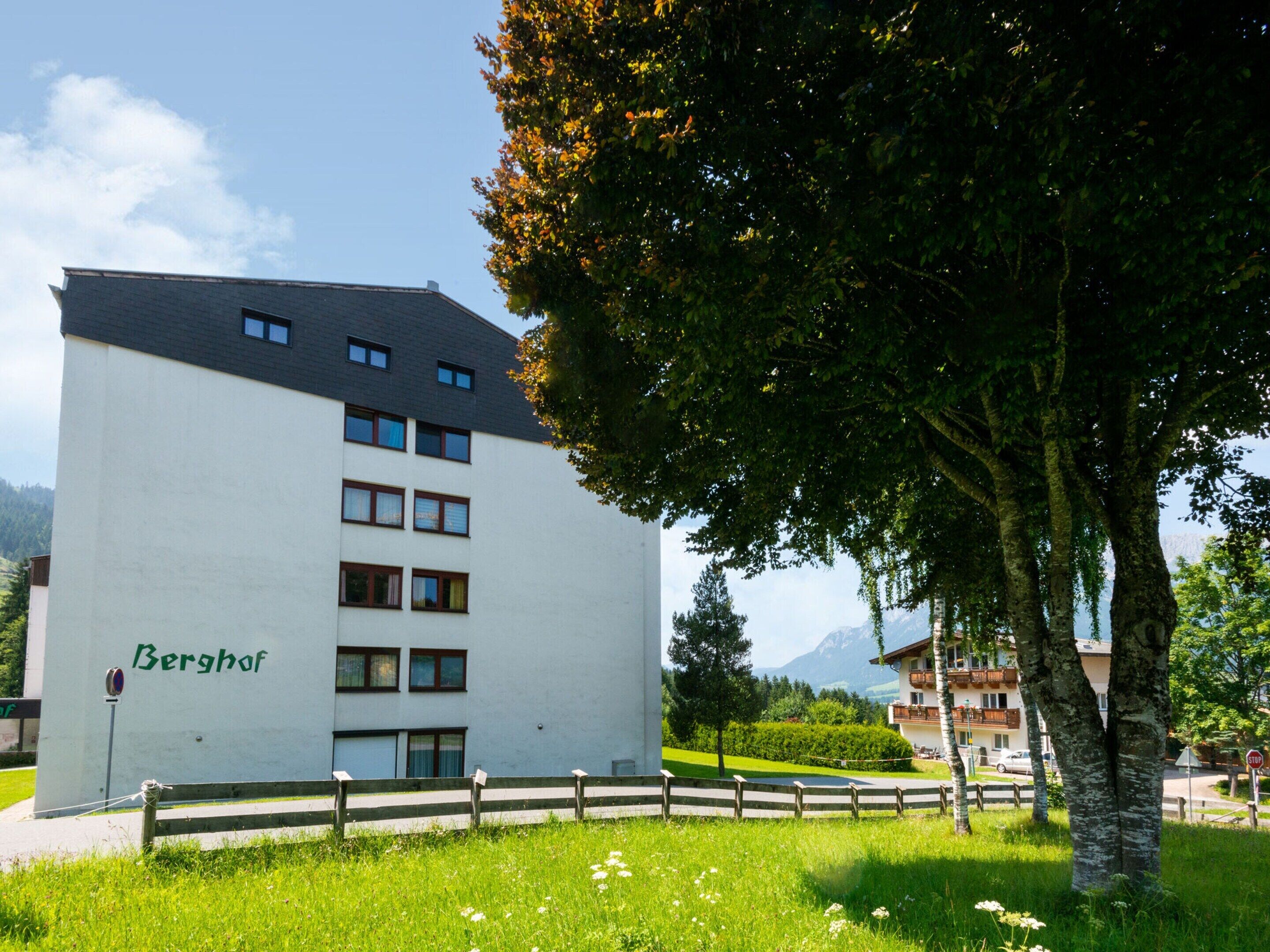 A multi-story building with a flat roof, labeled "Berghof," surrounded by lush greenery and a clear sky.