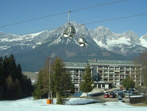 A ski resort with a mountain backdrop, a building with multiple floors, and a parking area. - Apartment in Ellmau With Ski-in Access (Ellmau)