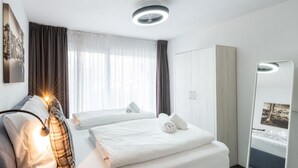 A modern hotel room with a bed, a wardrobe, a bedside table with a lamp, and a large mirror. - Apartment in Ellmau With Ski-in Access (Ellmau)