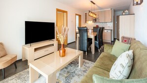 A modern living room with a flat-screen TV, a coffee table, and a sofa. There is a dining area with chairs and a kitchen in the background. - Apartment in Ellmau With Ski-in Access (Ellmau)