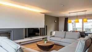 A modern living room with a flat-screen TV, grey sofas, a wooden coffee table, and pendant lighting. - Spacious Seaside Apartment (Nieuwpoort)