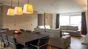 A modern living room with a dining area, grey sofas, a coffee table, and pendant lighting. - Spacious Seaside Apartment (Nieuwpoort)