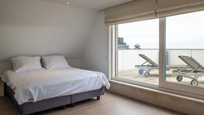 A bedroom with a bed, a large window, and a view of the cityscape. - Spacious Seaside Apartment (Nieuwpoort)