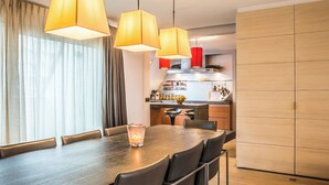 A modern dining area with a long table, multiple chairs, and pendant lighting. - Spacious Seaside Apartment (Nieuwpoort)