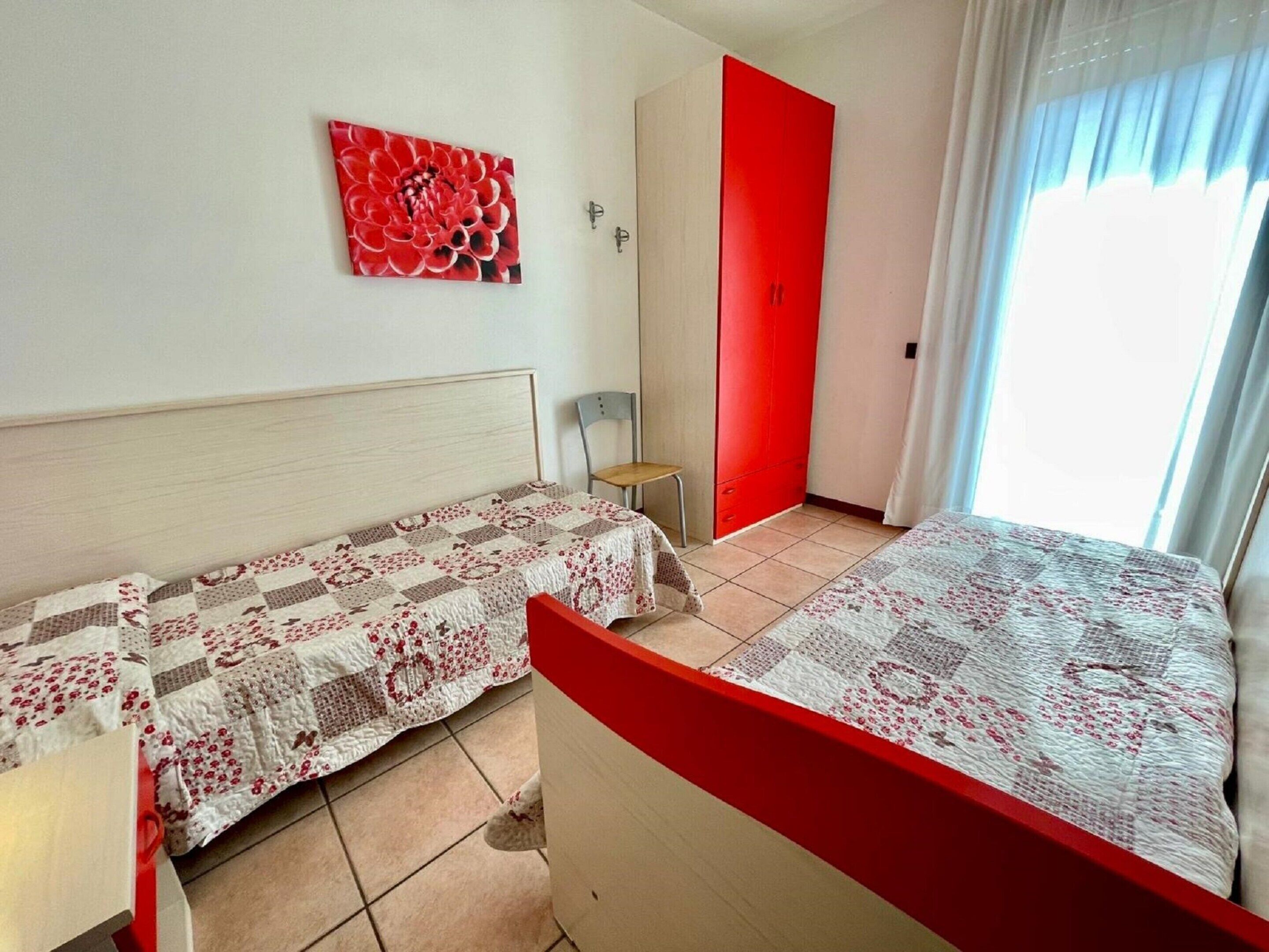 A bedroom with a bed, a chair, a red wardrobe, and a painting on the wall.