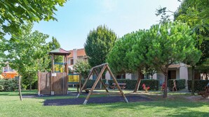 A playground with a swing set, a climbing structure, and a fenced play area. - Relaxing Apartment in Caorle for 7 (Caorle)