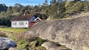 Ländliche Gegend mit einem weiß-roten Haus, umgeben von Bäumen und einem felsigen Hügel.