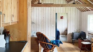 Ein gemütliches Blockhaus mit Holzwänden, einem Essbereich, einer Küche mit schwarzer Arbeitsplatte und einem Korbsessel.