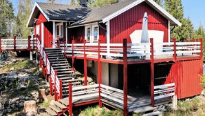 A red wooden house with a white porch and a staircase leading to a deck. - Holiday Home by the Lake (Tived)