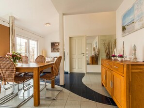 A dining area with a wooden table and wicker chairs, a wooden cabinet with decorative items, and a large mirror reflecting the room.