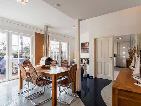 A modern dining area with a large table, wicker chairs, and a wood-burning pizza oven.
