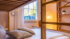A cozy room with a bed, a window with curtains, a wooden shelf with a plant, and a small table. - Seahorse Modern Retreat (Ostseebad Ahrenshoop)