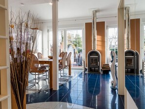A modern interior with a dining area, two fireplaces, and a large window providing natural light. - Seahorse Modern Retreat (Ostseebad Ahrenshoop)