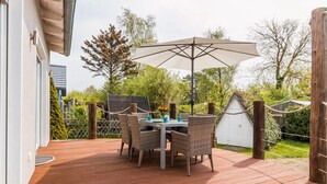 An outdoor patio with a table and chairs, a large umbrella, and a wooden deck. - Seahorse Modern Retreat (Ostseebad Ahrenshoop)