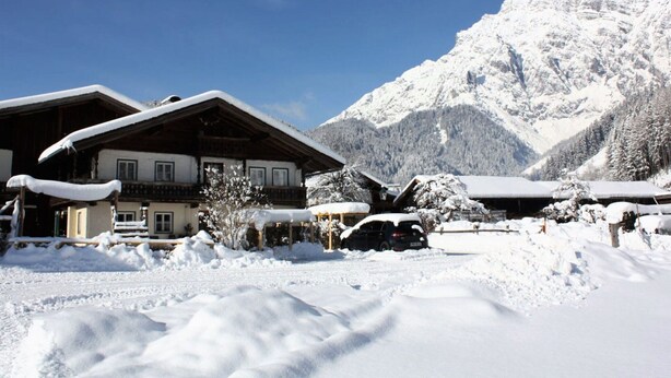 Un chalet de montagne enneigé, doté d’une architecture traditionnelle en bois, sous un ciel bleu azur, avec une montagne enneigée en arrière-plan.