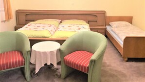 Une chambre à coucher avec un lit, deux chaises, une petite table et deux tableaux encadrés accrochés au mur.