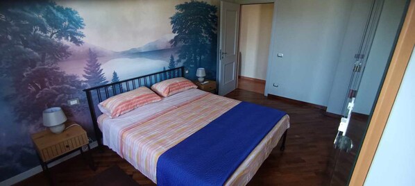 A bedroom with a bed, a nightstand, a lamp, and a mural on the wall.