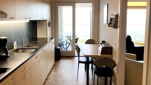A compact kitchen with a dining area, a view through the door, and a small table with chairs. - Apartment in Nieuwpoort With sea Beach (Nieuwpoort)