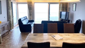 A hotel room with a dining area, a sofa, a TV, and large windows with curtains. - Apartment in Nieuwpoort With sea Beach (Nieuwpoort)