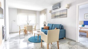 A modern living room with a blue sofa, a coffee table, and a dining area with chairs and a table.