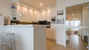 Una cocina moderna con armarios blancos, un microondas integrado y una pequeña isla con taburetes.
