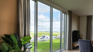 A modern hotel room with large windows, a grey sofa, and a potted plant. - Villa in Leons Near Frisian Lakes (Leons)