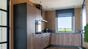 A modern kitchen with wooden cabinets, a built-in oven, and a window with a view of the outdoors. - Villa in Leons Near Frisian Lakes (Leons)