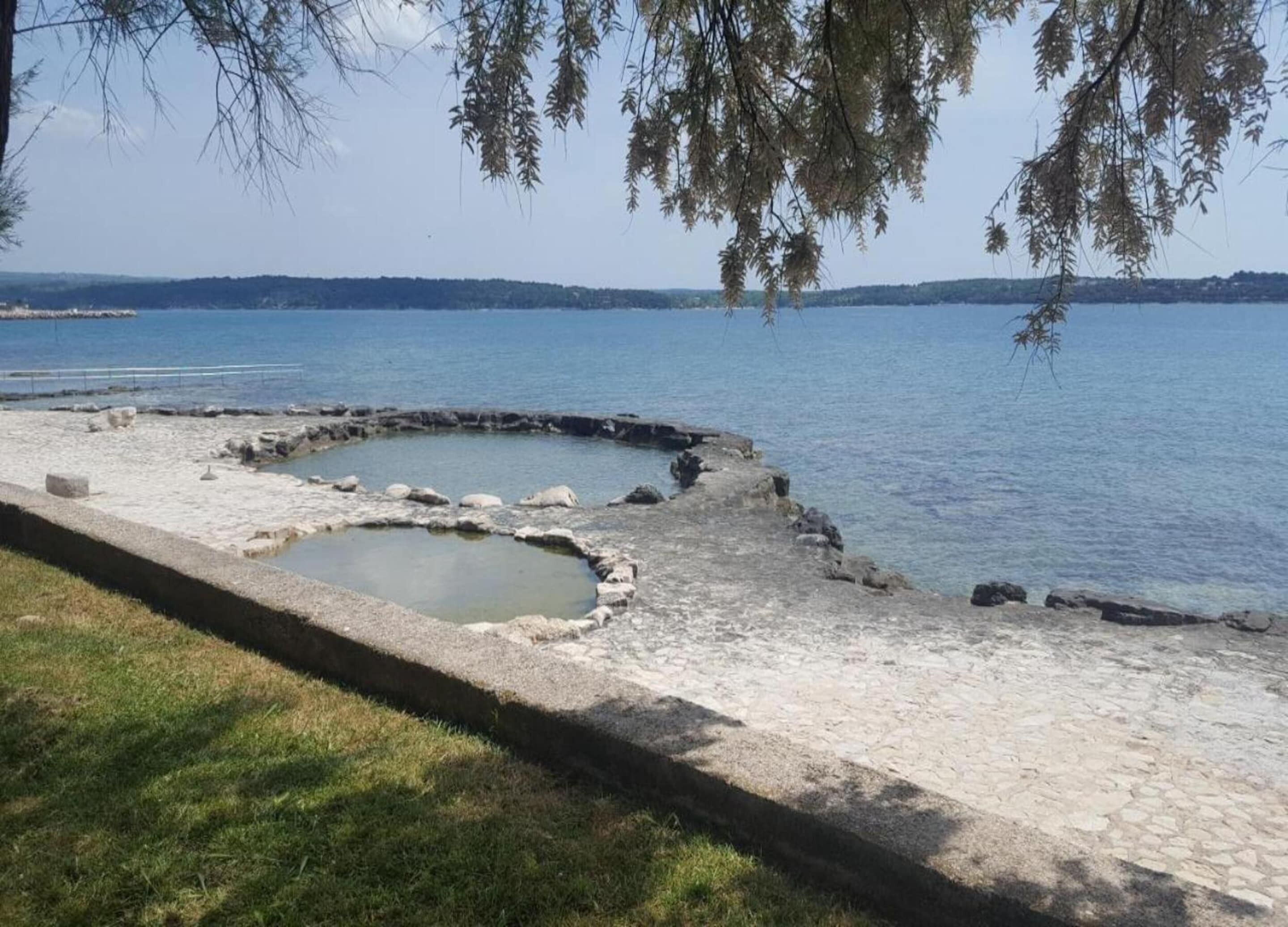 A stone pathway leading to a circular water feature by a lake.