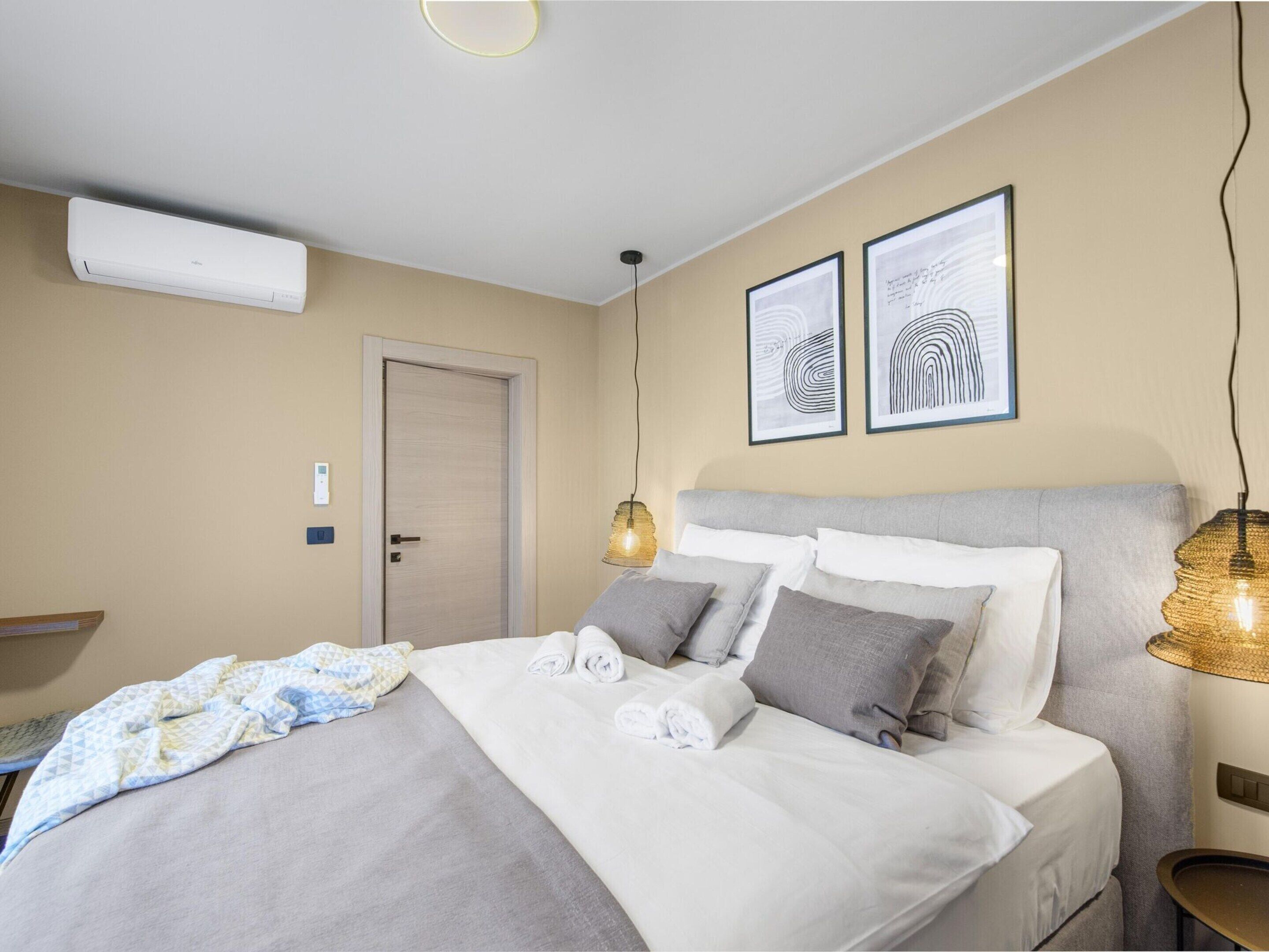 A neatly made bed with pillows and a blanket, a bedside lamp, and two framed artworks on the wall.