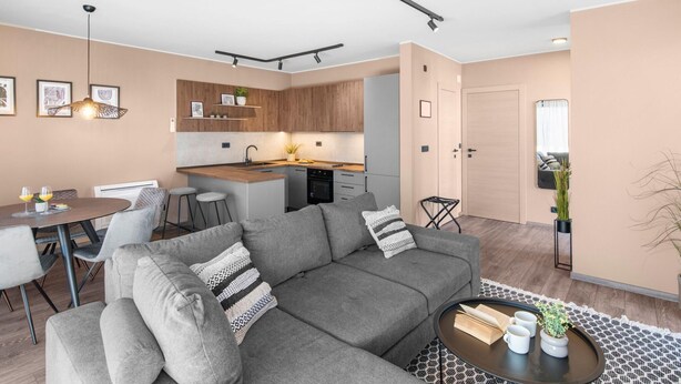 Un salon moderne avec un canapé gris, une table à manger avec des chaises, un coin cuisine doté de meubles en bois et un petit îlot avec un évier.