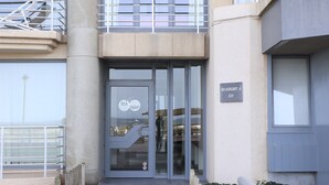 A building entrance with a glass door, a metal railing, and a sign indicating the name and address. - Seafront Apartment in Nieuwpoort Marina (Nieuwpoort)