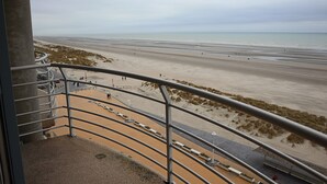 A balcony with a view of a beach, featuring a metal railing and a paved walkway. - Seafront Apartment in Nieuwpoort Marina (Nieuwpoort)
