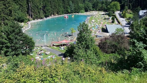 A large outdoor swimming pool surrounded by dense forest, with a few buildings and a road nearby. - Chalet Brilon Modern Retreat (Brilon)