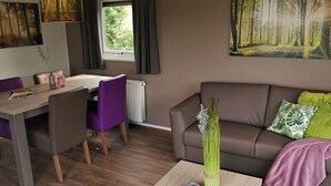 A modern living room with a brown sofa, purple chairs, a dining table, and a large forest-themed painting on the wall. - Chalet Brilon Modern Retreat (Brilon)