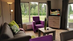 A living room with a sofa, a purple armchair, a coffee table, and a TV on a wooden cabinet. - Chalet Brilon Modern Retreat (Brilon)