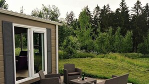 A patio with wicker furniture, a glass door, and a grassy area with trees. - Chalet Brilon Modern Retreat (Brilon)