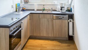 Eine kompakte Küche mit Holzschränken, einem Einbauofen, einem Geschirrspüler und einem Fenster über der Spüle.