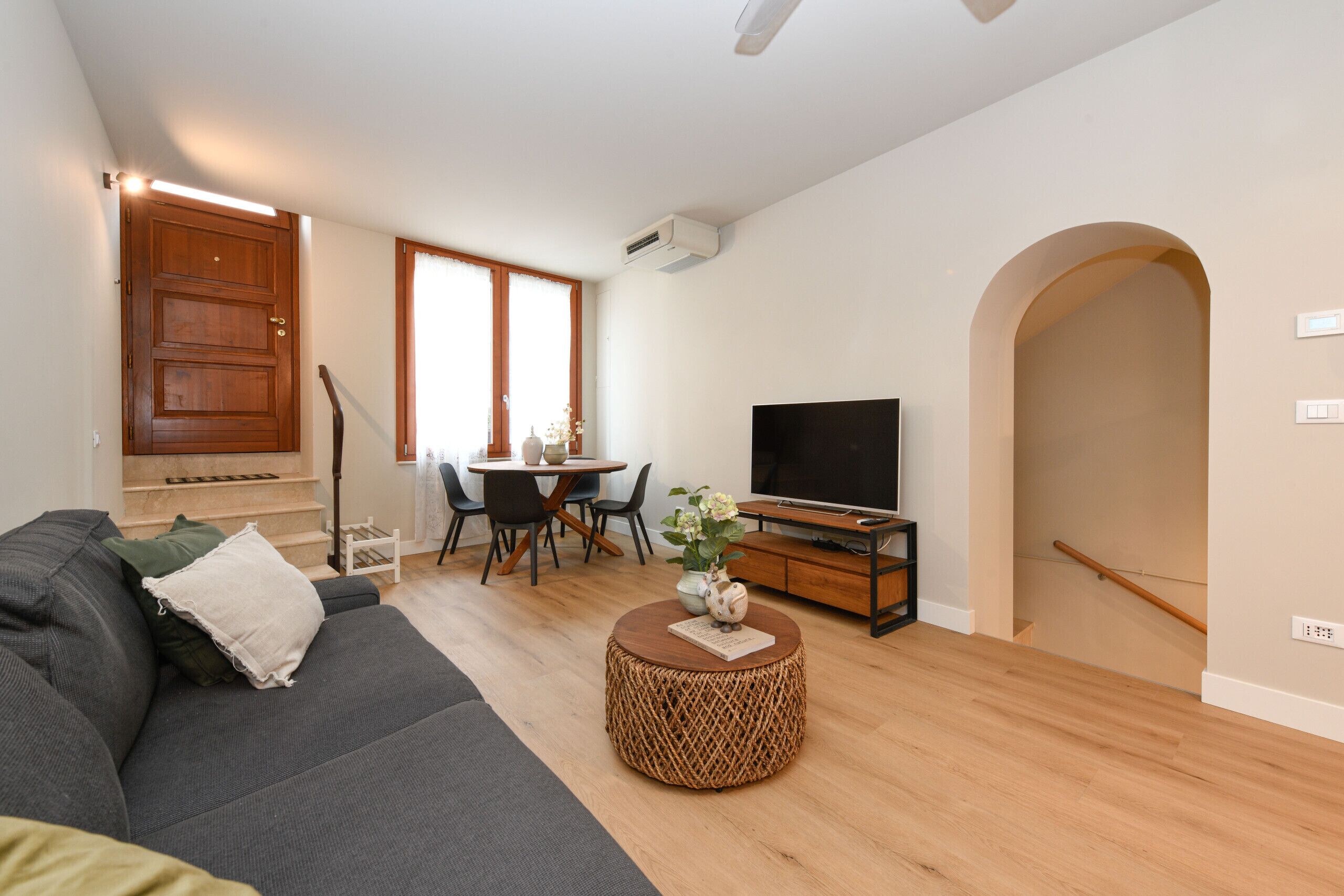 A modern living room with a sofa, a coffee table, a TV, and a dining area with chairs and a table.