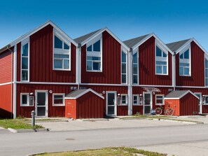 Un immeuble rouge à plusieurs étages, orné de moulures blanches, avec des portes numérotées et de grandes fenêtres.
