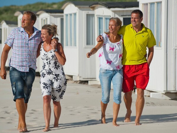 Une famille se promène sur un sentier sablonneux, avec des cabanes de plage en arrière-plan.